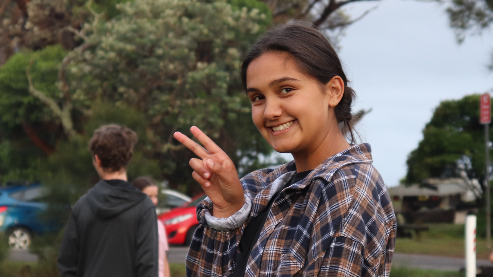 A young adult volunteer smiling outside and holding up a peace sign with two fingers